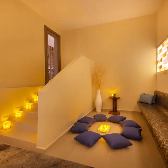 Dimly lit meditation area with circle of cushions and glowing candles for peaceful, ambient spa relaxation.