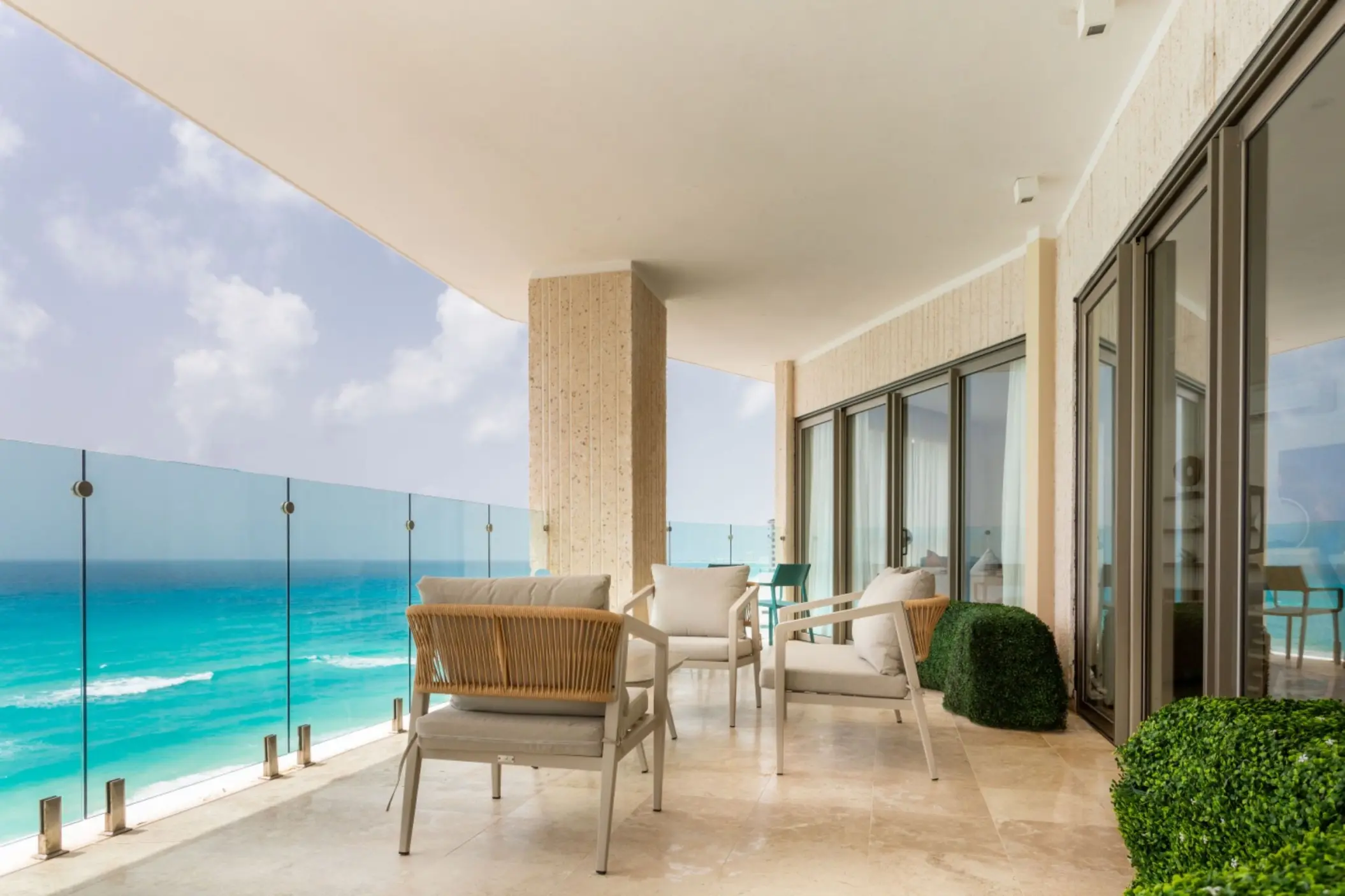 Expansive balcony of a suite with outdoor seating and a glass railing overlooking the Caribbean Sea.