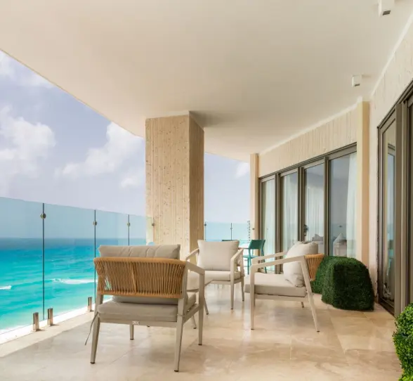 Expansive balcony of a suite with outdoor seating and a glass railing overlooking the Caribbean Sea.