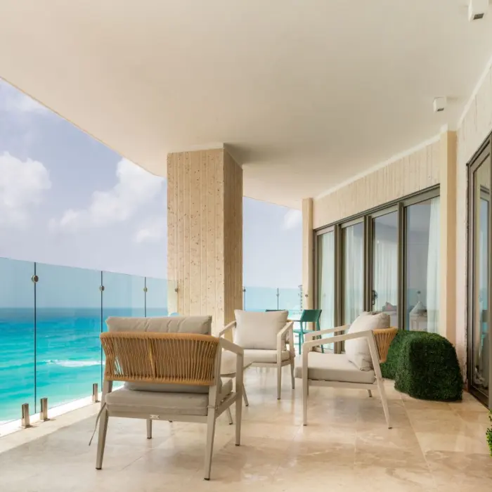 Expansive balcony of a suite with outdoor seating and a glass railing overlooking the Caribbean Sea.