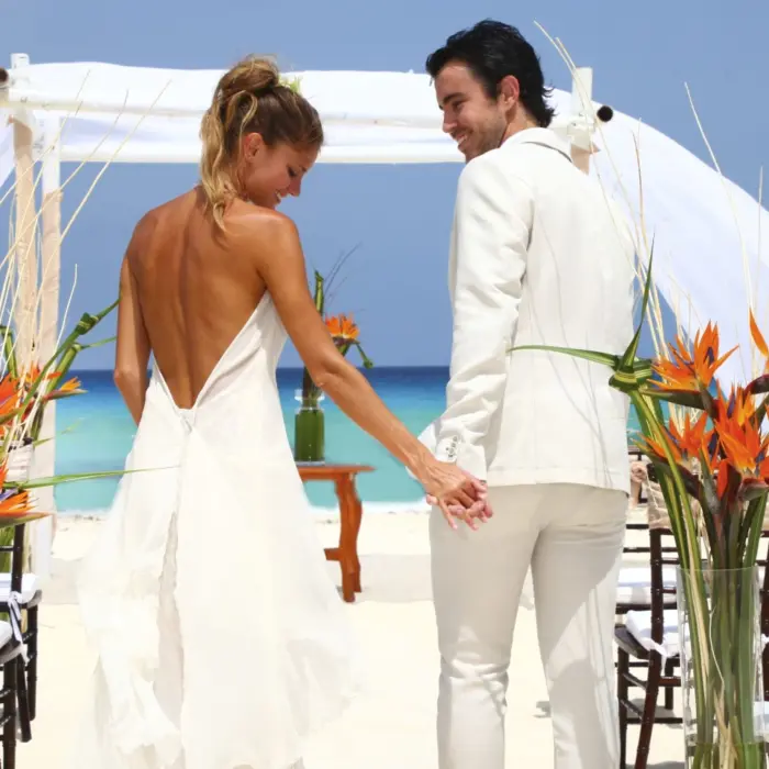 A bride and groom holding hands and walking on a white sand beach toward a wedding arch.
