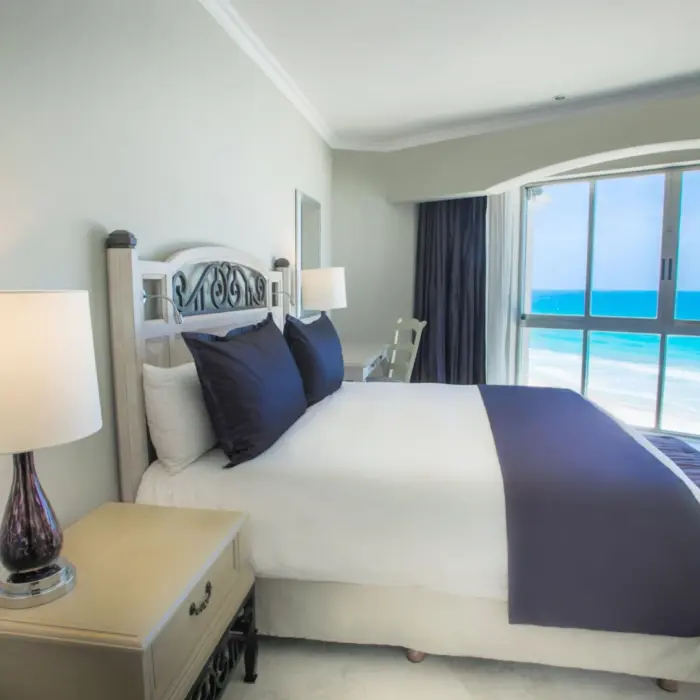 Bedroom with a king-sized bed and a large window offering a panoramic view of the turquoise ocean.