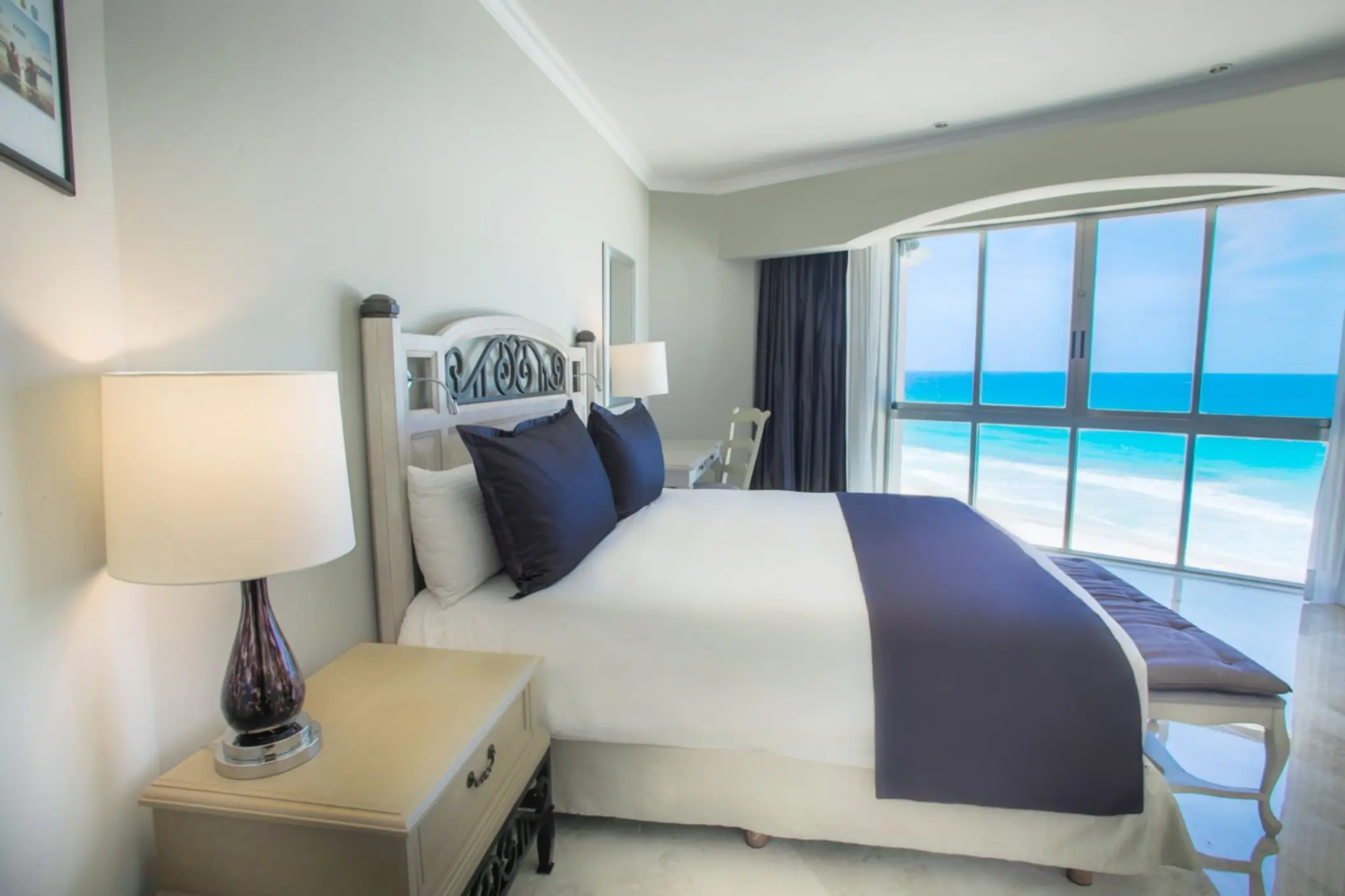 Bedroom with a king-sized bed and a large window offering a panoramic view of the turquoise ocean.