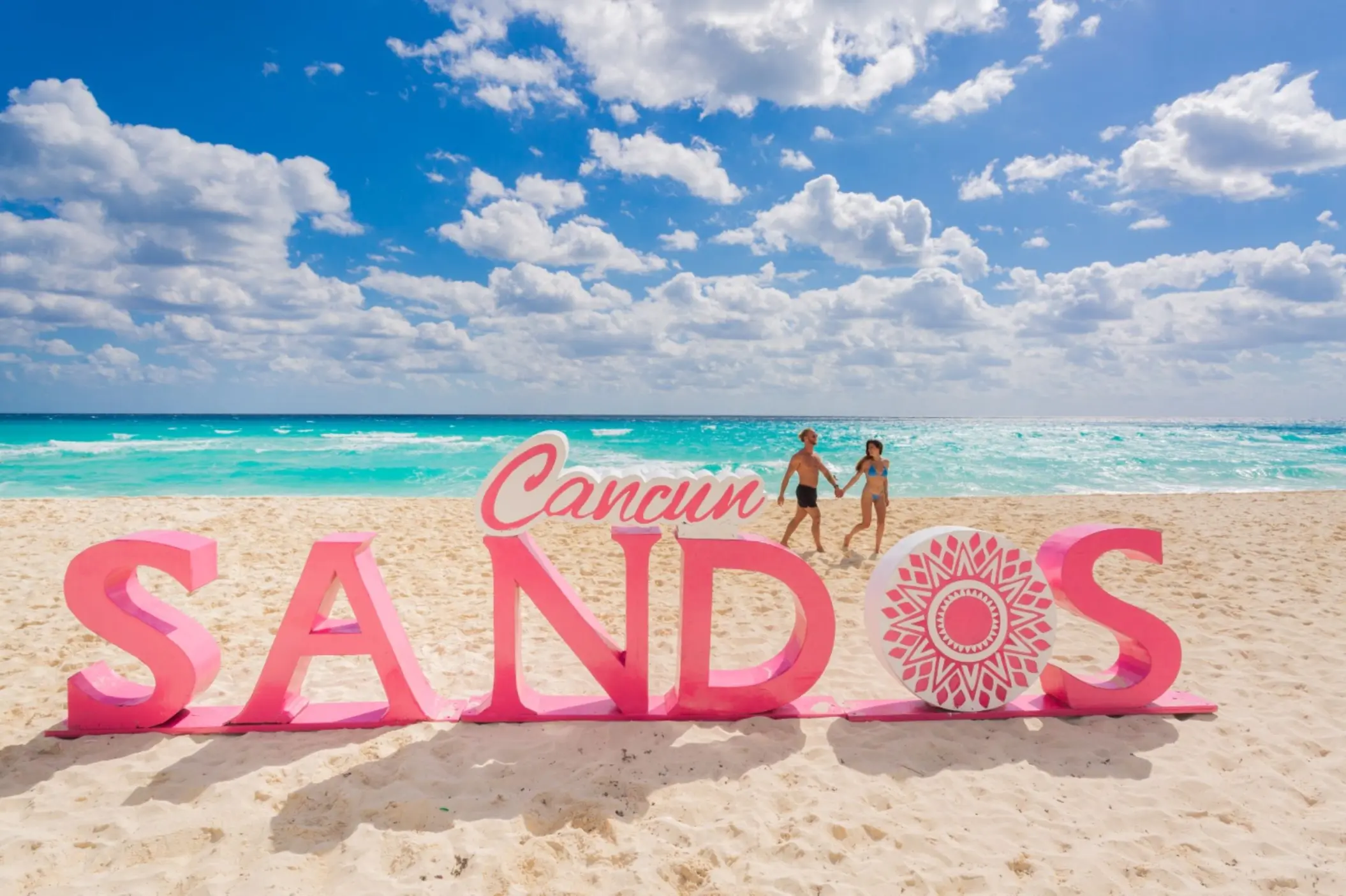 A couple holding hands and walking on a sandy beach next to a large pink 