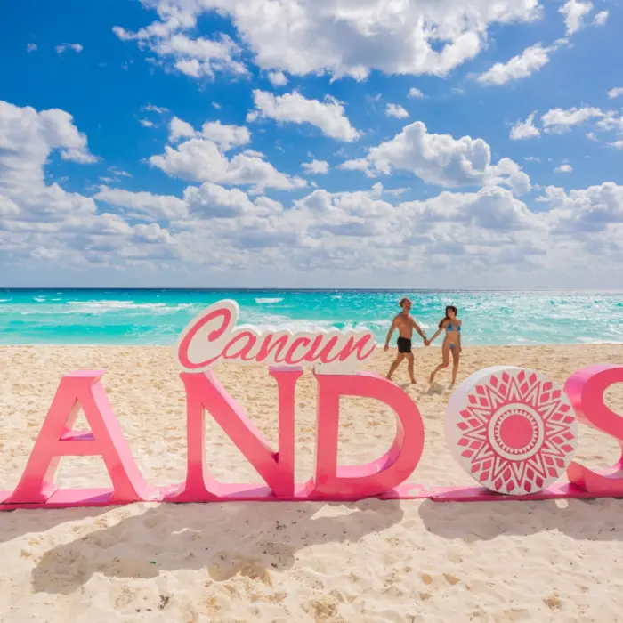 A couple holding hands and walking on a sandy beach next to a large pink 