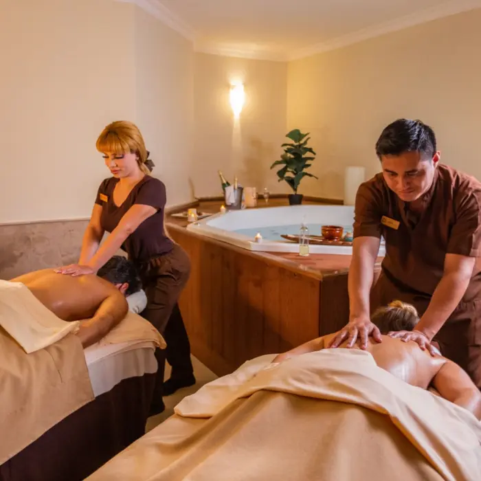 A couple receiving a relaxing massage side-by-side in a tranquil, dimly lit spa room.