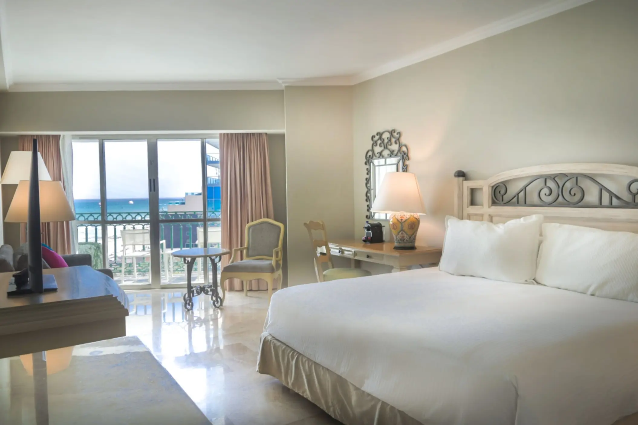 A spacious deluxe suite with a large bed, a desk area, and a balcony overlooking the ocean.