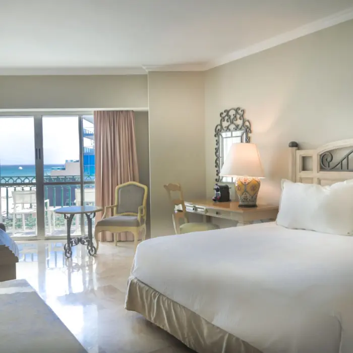 A spacious deluxe suite with a large bed, a desk area, and a balcony overlooking the ocean.