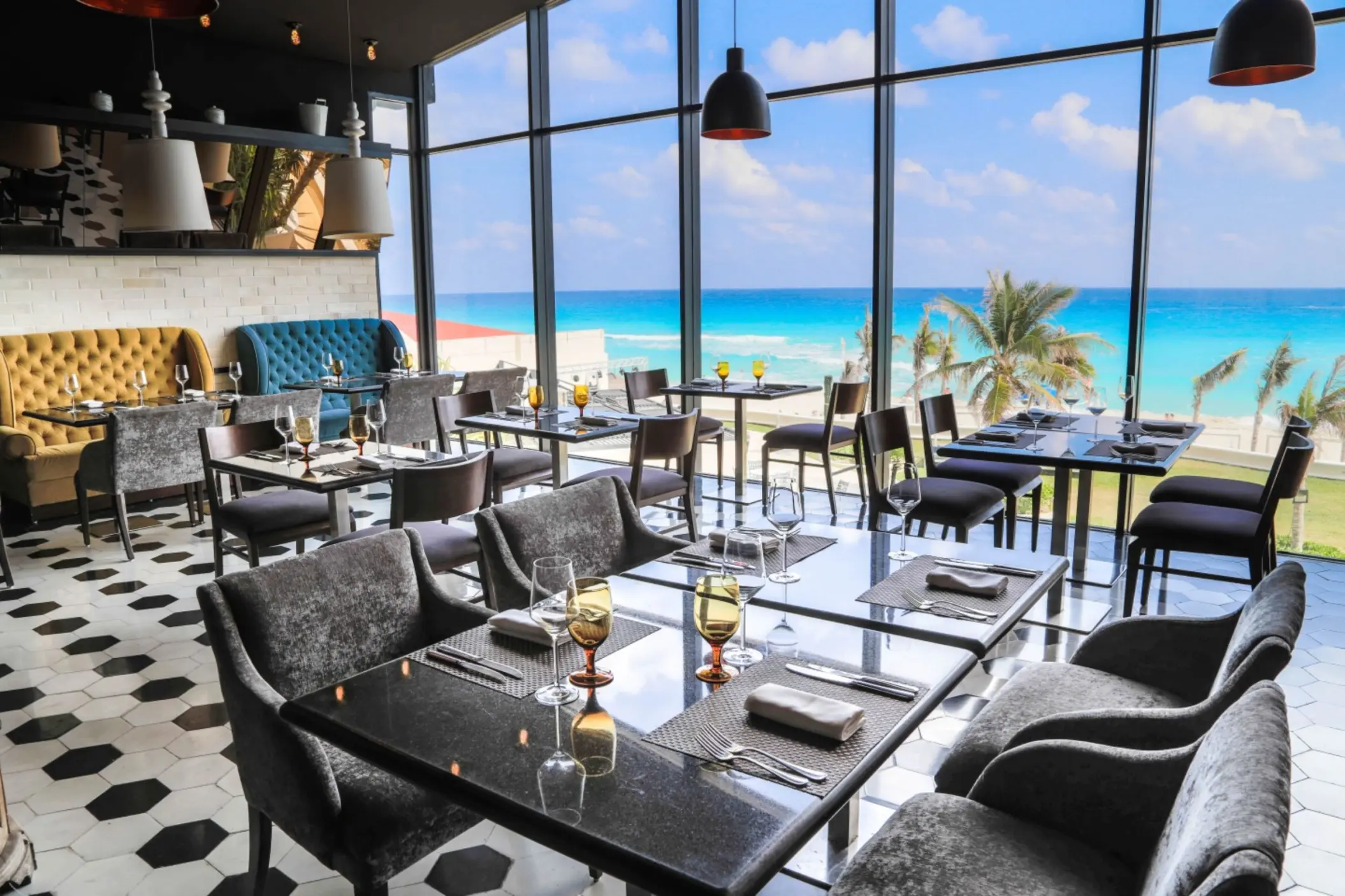 A modern restaurant dining room with floor-to-ceiling windows and tables overlooking the beach and ocean.
