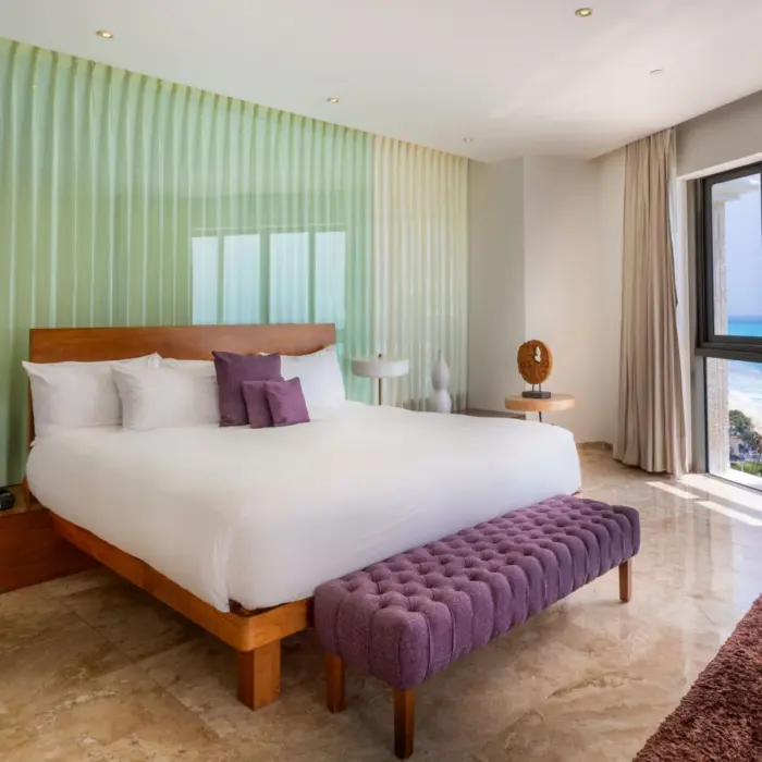 Modern king bedroom with a purple ottoman, marble floor, and floor-to-ceiling windows with an ocean view.