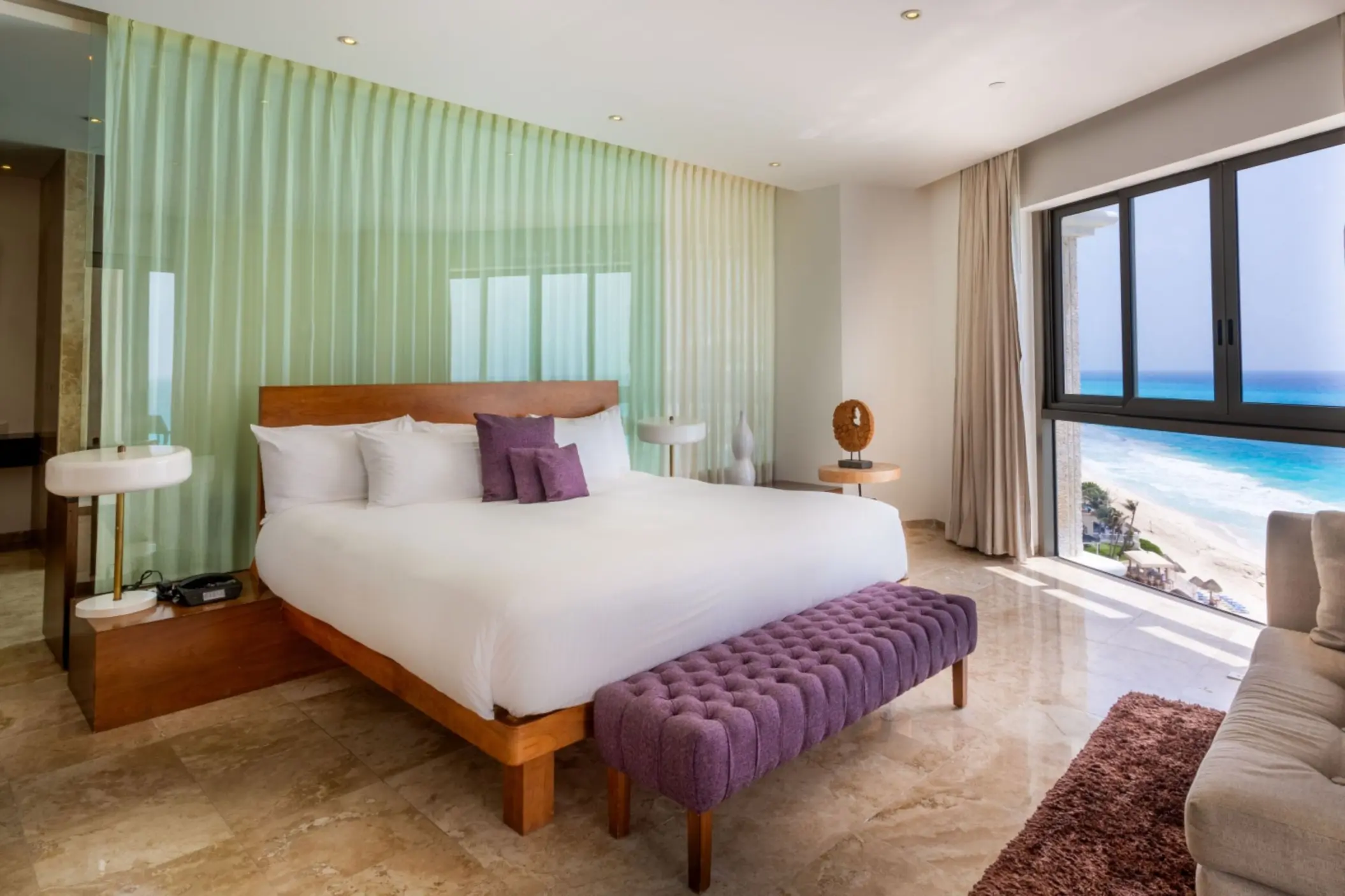 Modern king bedroom with a purple ottoman, marble floor, and floor-to-ceiling windows with an ocean view.