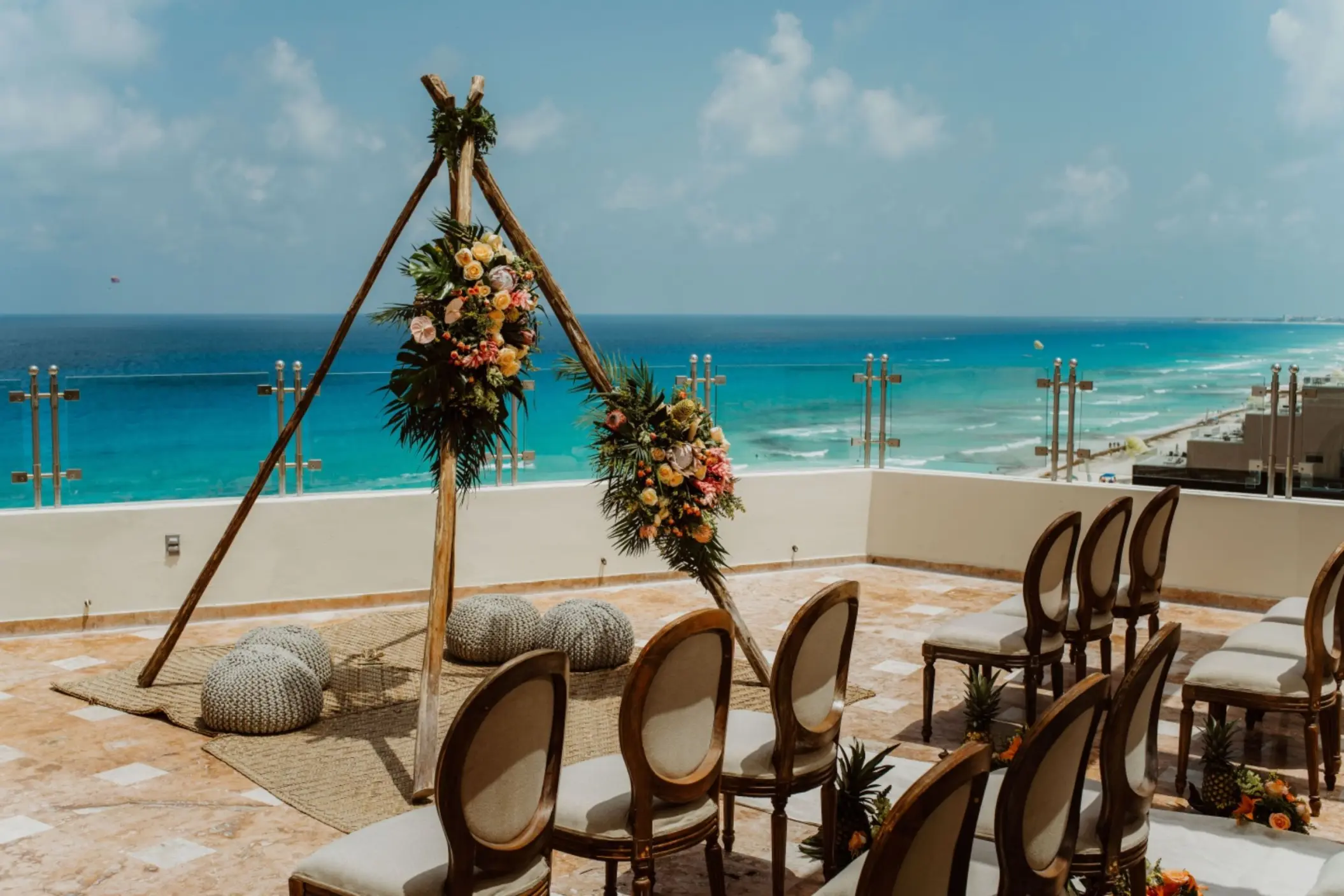 A rooftop wedding setup featuring a rustic floral arch, chiavari chairs, and a panoramic ocean view.