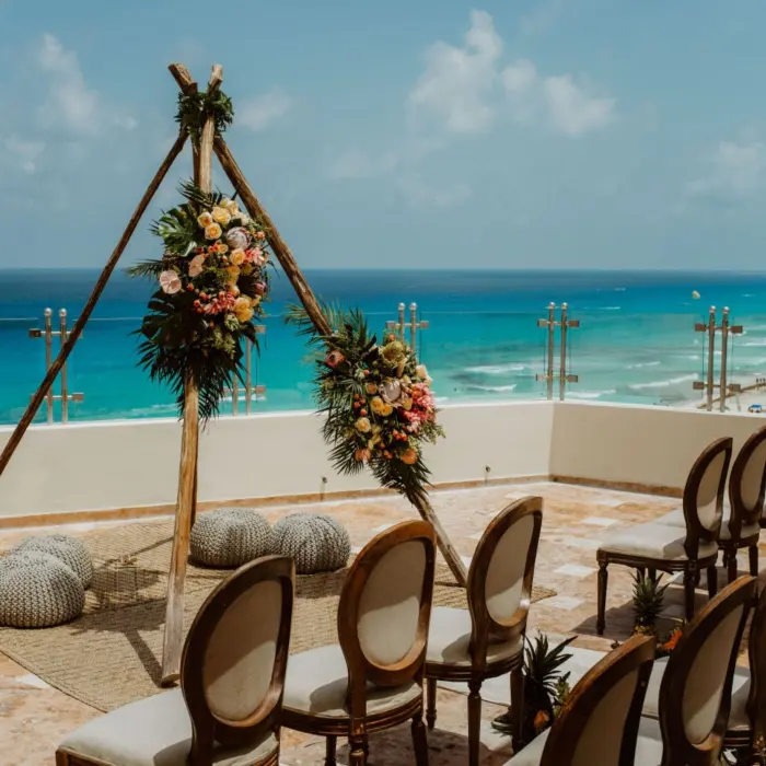 A rooftop wedding setup featuring a rustic floral arch, chiavari chairs, and a panoramic ocean view.