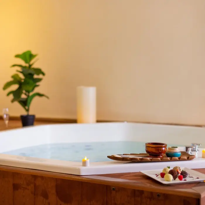 A luxurious spa hot tub decorated with lit candles, champagne, and a small platter of chocolates.