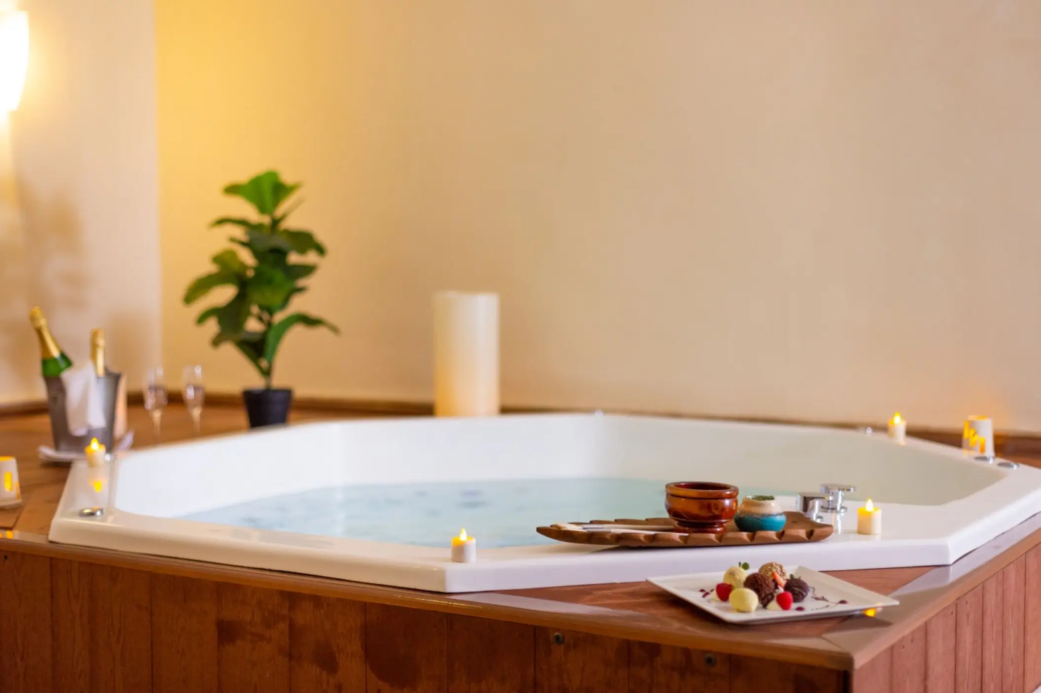 A luxurious spa hot tub decorated with lit candles, champagne, and a small platter of chocolates.