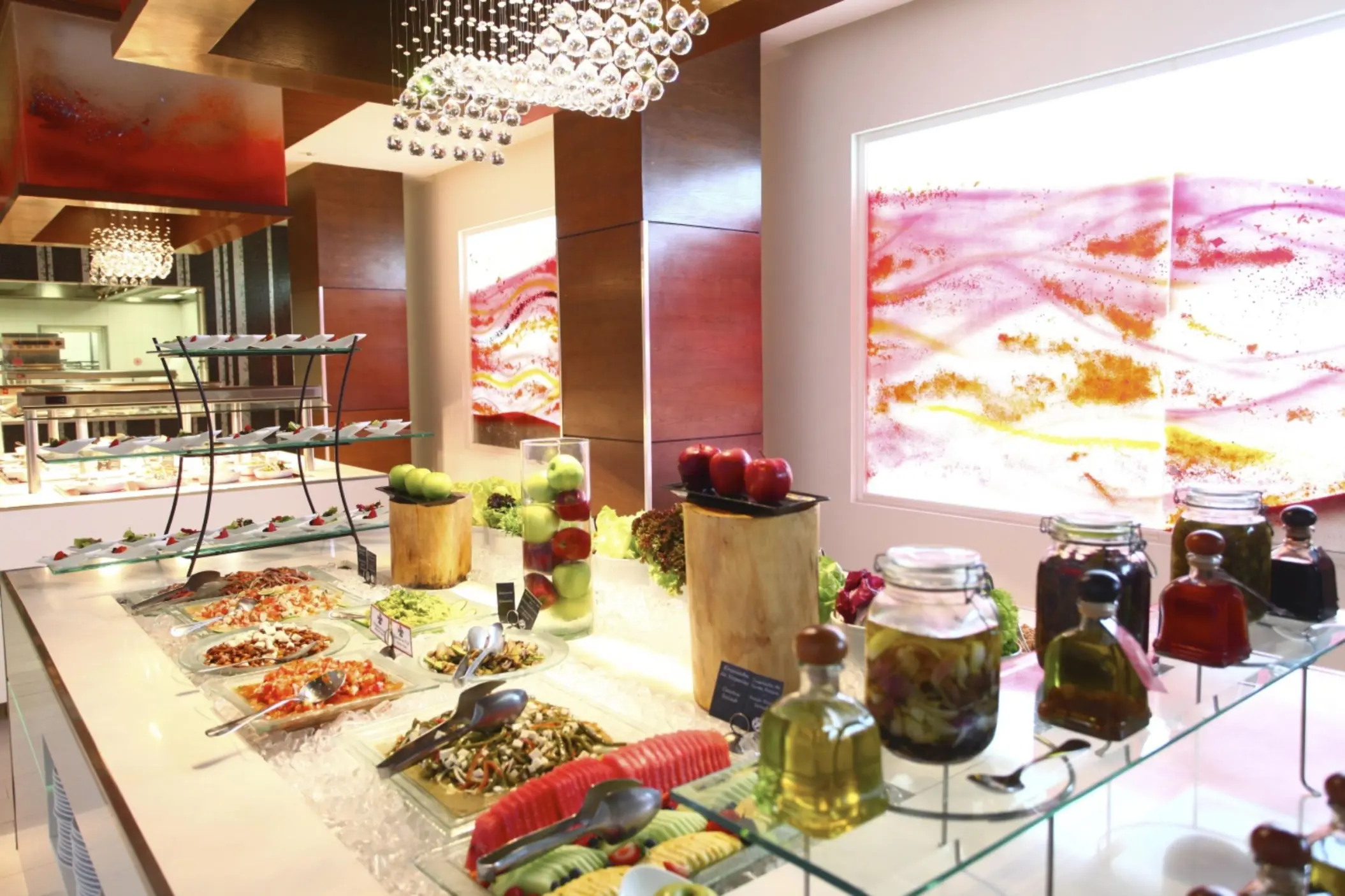 A brightly lit restaurant with a modern buffet spread of salads, vegetables, and fresh fruit.