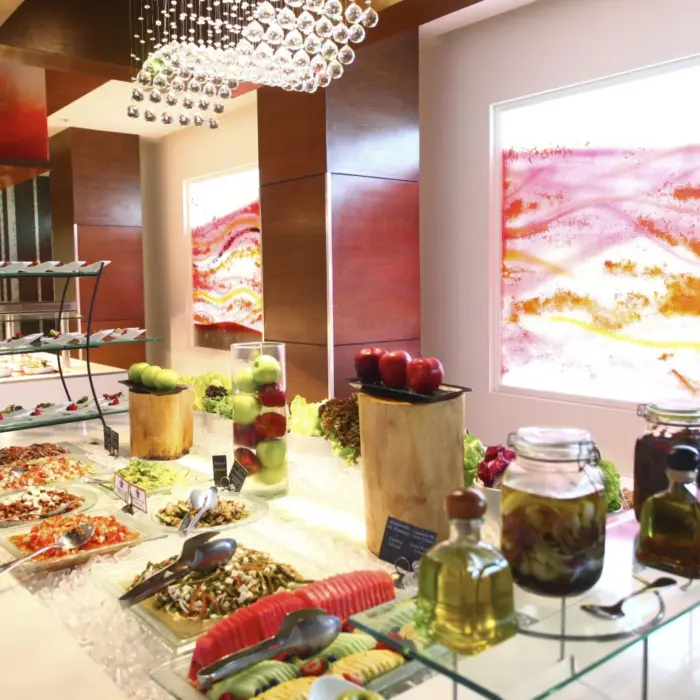 A brightly lit restaurant with a modern buffet spread of salads, vegetables, and fresh fruit.