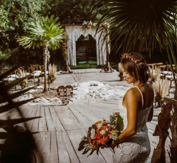 A radiant bride in a white dress and flower crown smiles at the cenote wedding venue.