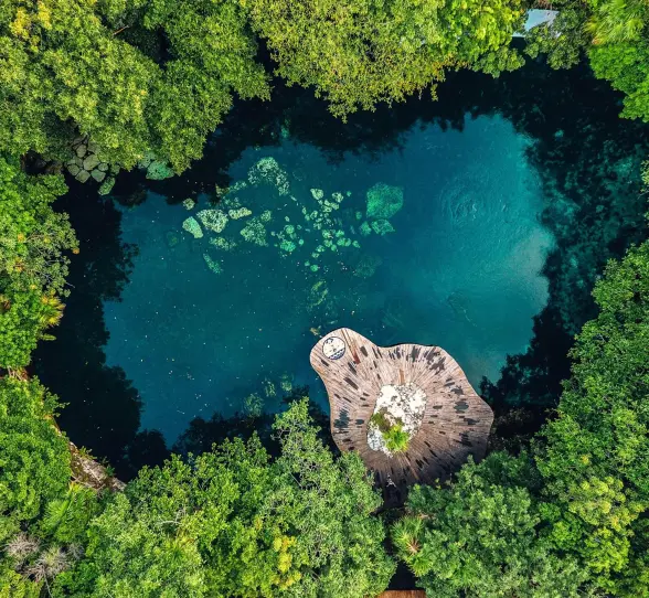 An aerial view of a vibrant blue cenote surrounded by dense green trees at Sandos Caracol Eco Resort.