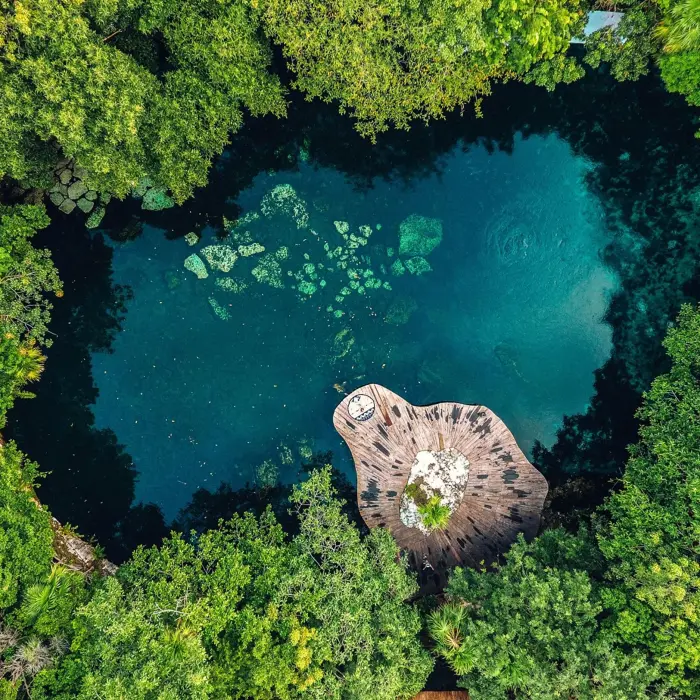 An aerial view of a vibrant blue cenote surrounded by dense green trees at Sandos Caracol Eco Resort.