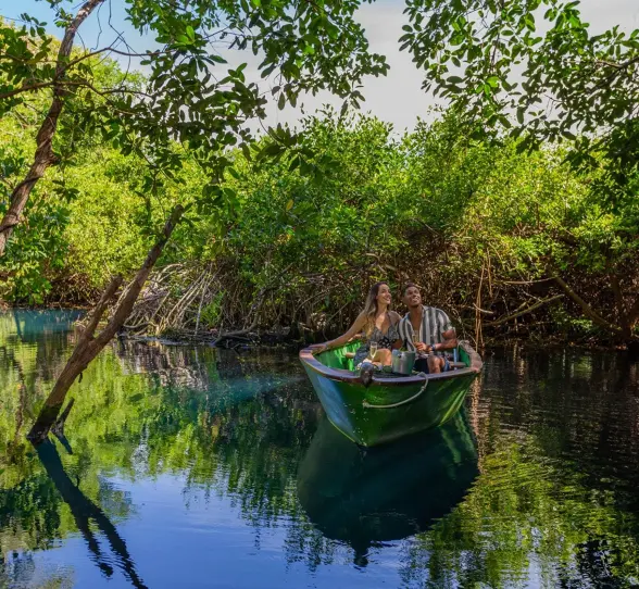 A couple enjoys a peaceful boat ride through lush green mangroves at Sandos Caracol Eco Resort.