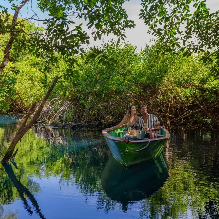 A couple enjoys a peaceful boat ride through lush green mangroves at Sandos Caracol Eco Resort.