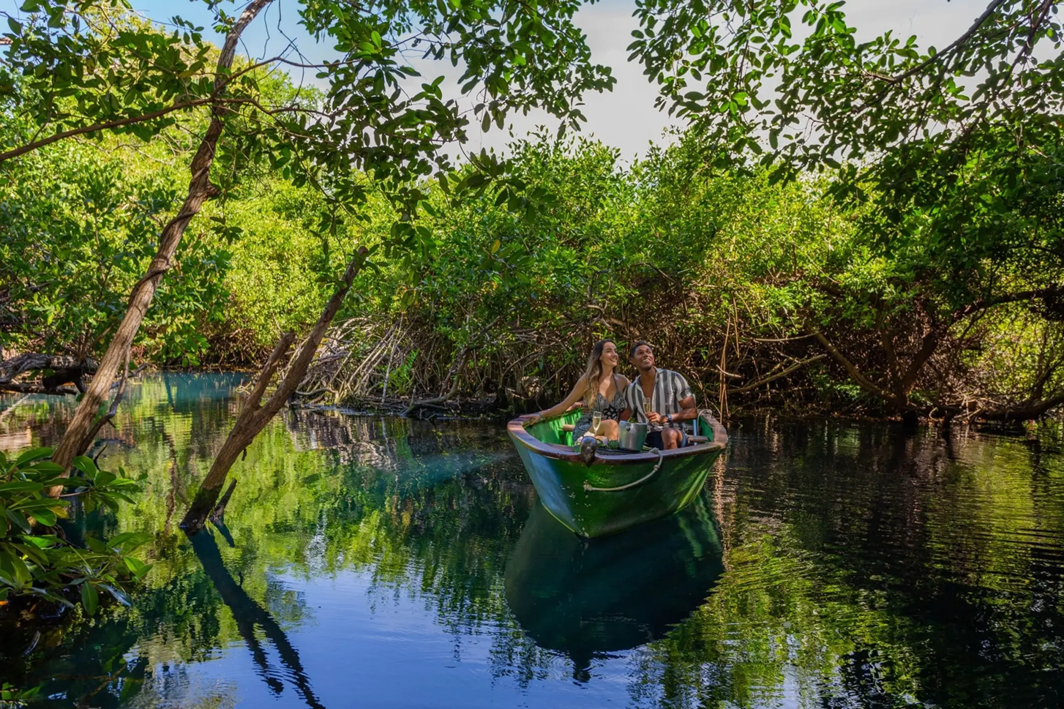 A couple enjoys a peaceful boat ride through lush green mangroves at Sandos Caracol Eco Resort.