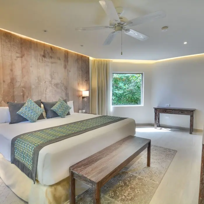 A spacious, modern penthouse suite at Sandos Caracol Eco Resort with a large bed, wooden wall, and ceiling fan.