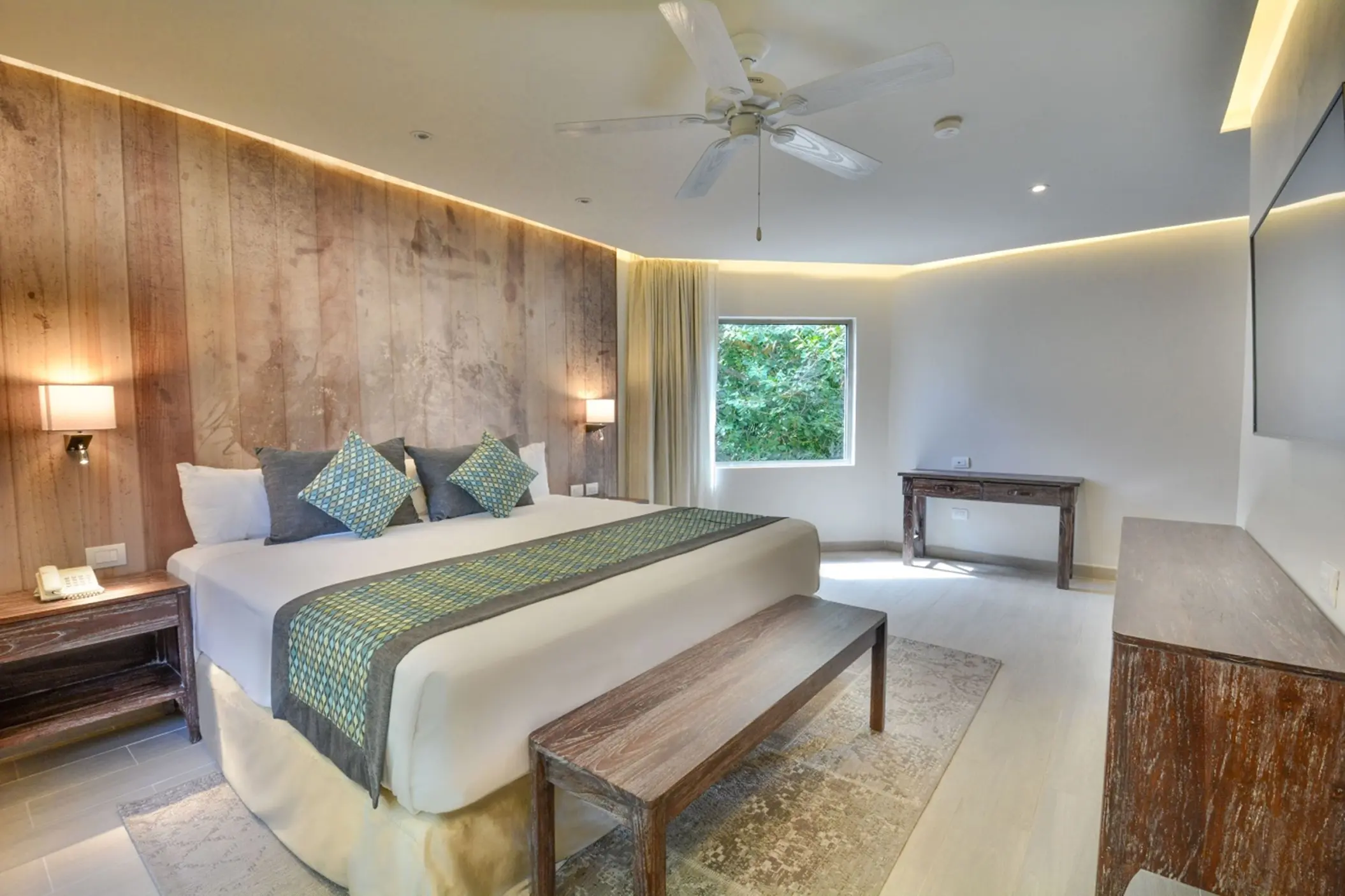 A spacious, modern penthouse suite at Sandos Caracol Eco Resort with a large bed, wooden wall, and ceiling fan.