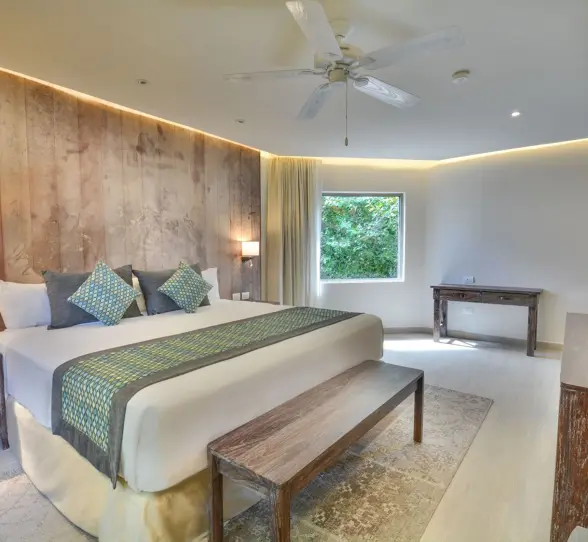 A spacious, modern penthouse suite at Sandos Caracol Eco Resort with a large bed, wooden wall, and ceiling fan.
