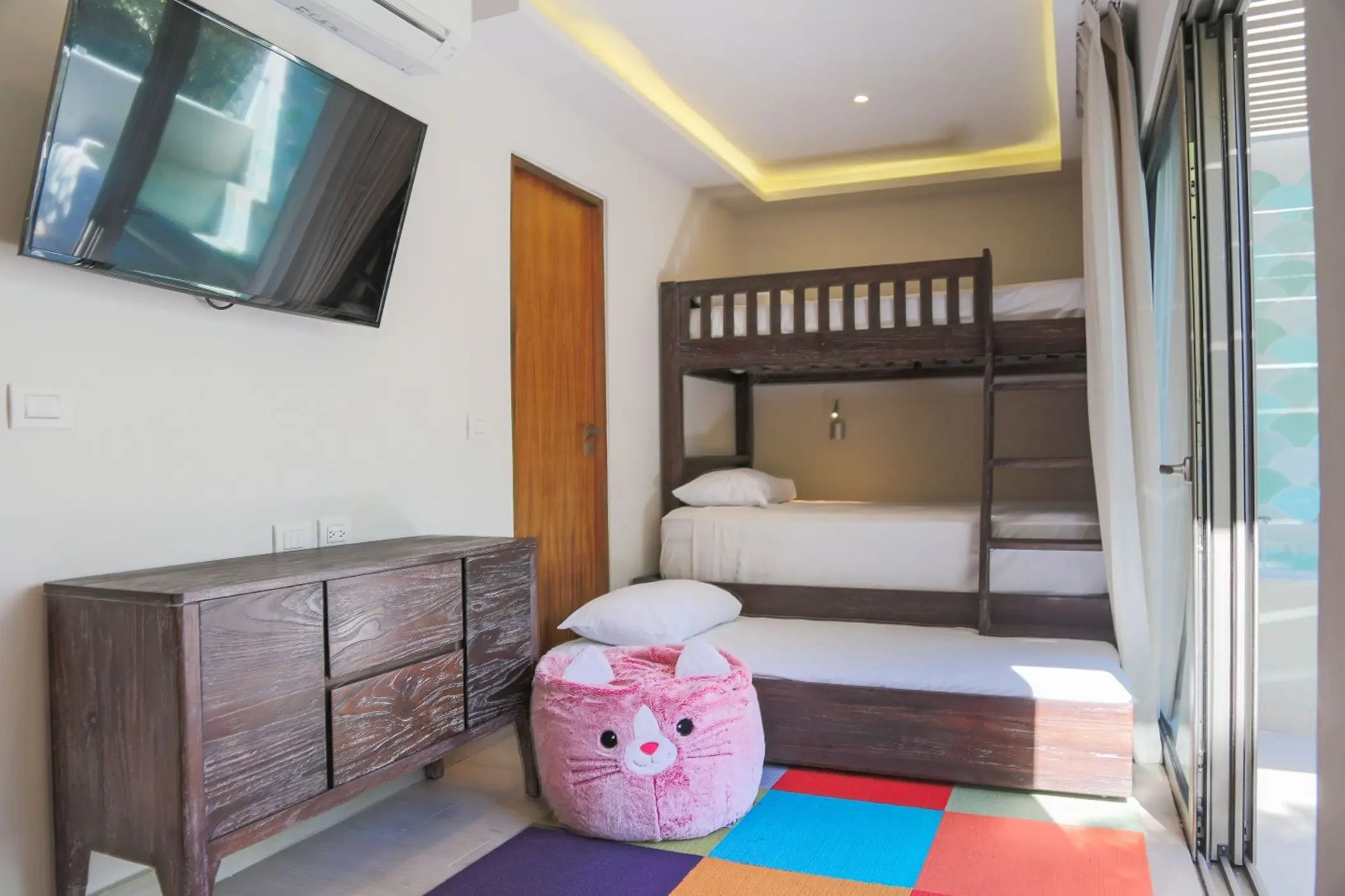 A bright family suite at Sandos Caracol Eco Resort with bunk beds, a TV, and a colorful playmat.