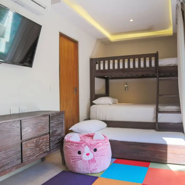 A bright family suite at Sandos Caracol Eco Resort with bunk beds, a TV, and a colorful playmat.