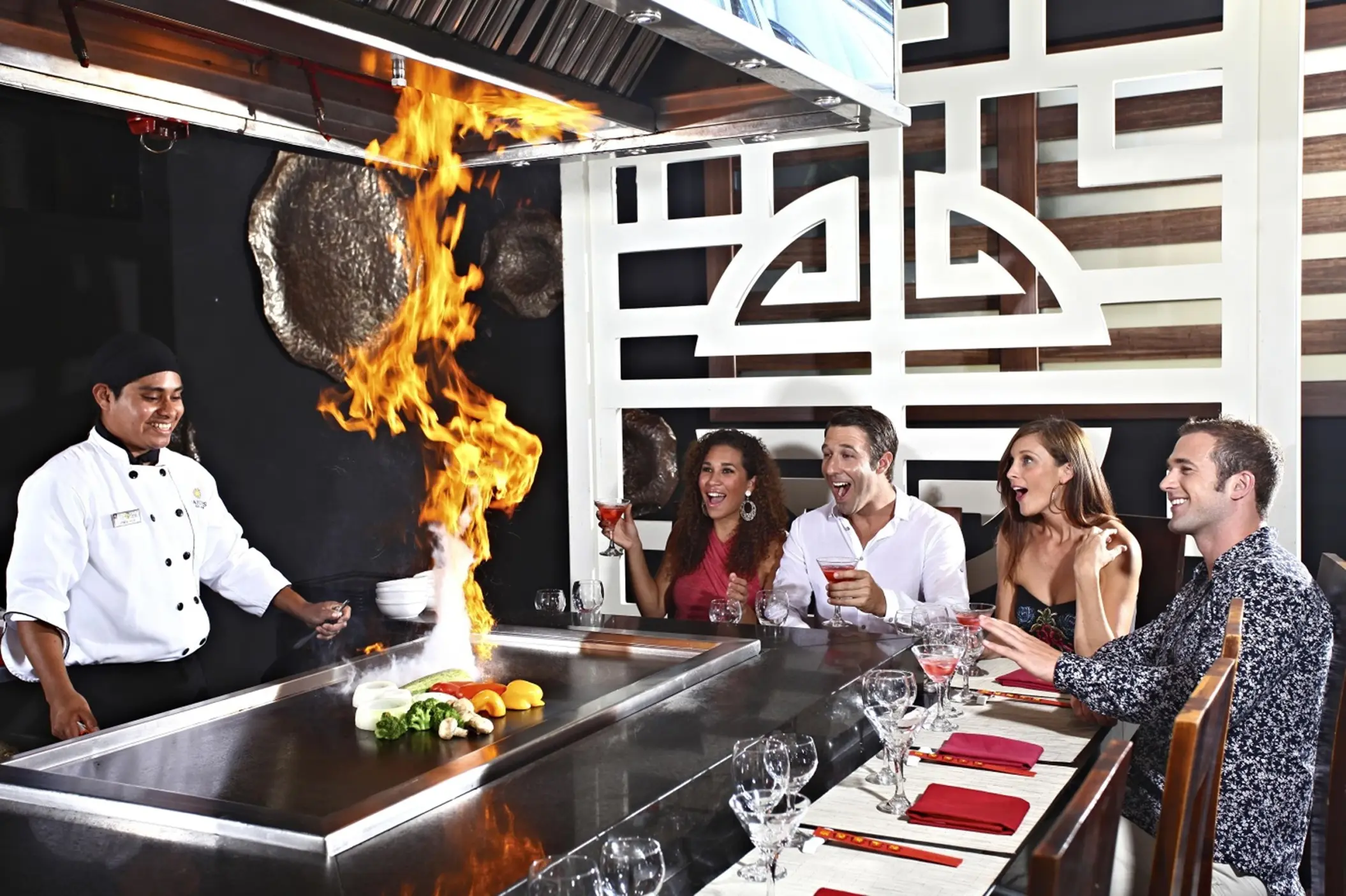 A chef flambés food at a teppanyaki grill for smiling diners at Templo restaurant, Sandos Caracol.