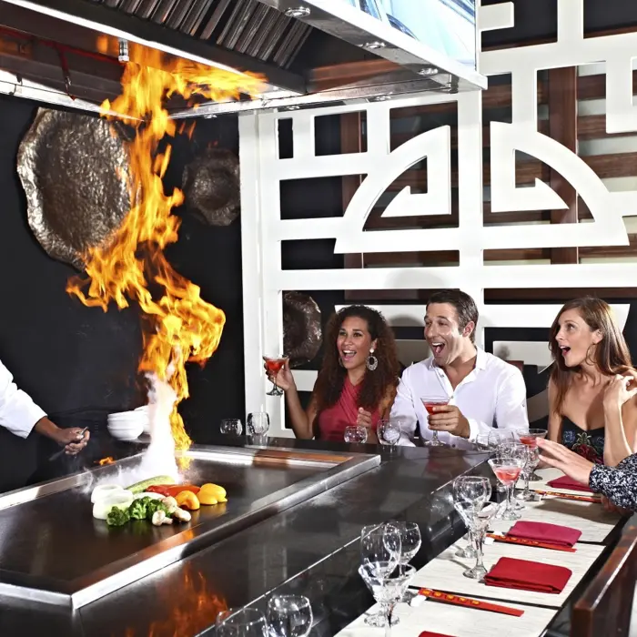 A chef flambés food at a teppanyaki grill for smiling diners at Templo restaurant, Sandos Caracol.