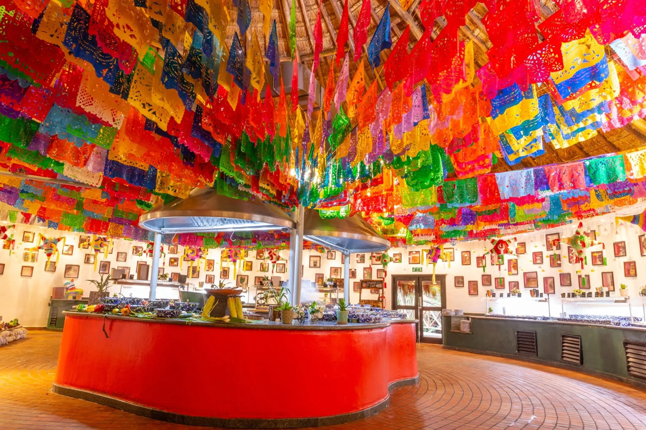 Mascaras restaurant at Sandos Caracol Eco Resort features colorful papel picado decorations and a central buffet.