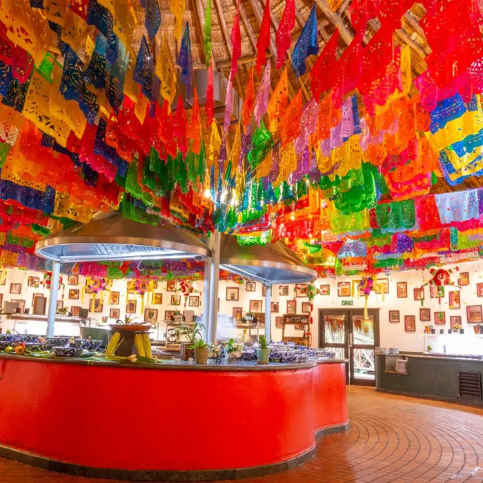 Mascaras restaurant at Sandos Caracol Eco Resort features colorful papel picado decorations and a central buffet.