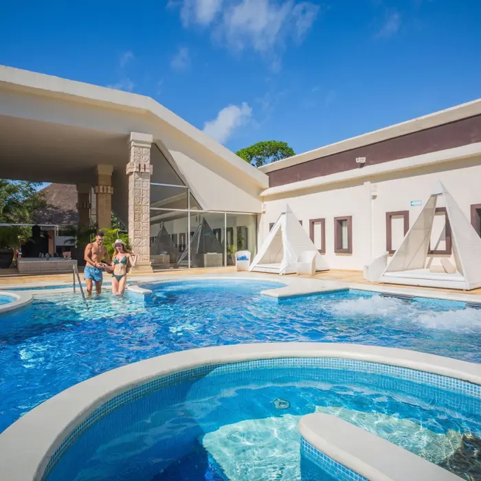 A couple enjoys a large, inviting pool area with cabanas and modern architecture at Sandos Caracol.