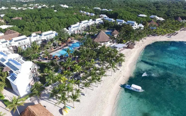 An aerial view of Sandos Caracol Eco Resort showing beachfront buildings, pools, and lush green areas.