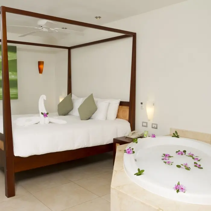 A suite at Sandos Caracol Eco Resort features a four-poster bed and a luxurious tub with flower petals.