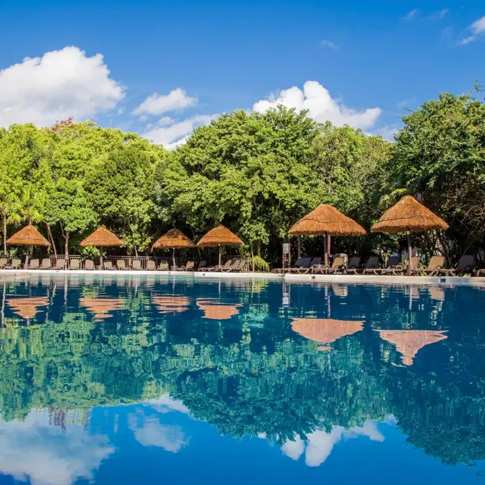 The Tortuga pool at Sandos Caracol Eco Resort, with clear blue water reflecting palm trees and cabanas.