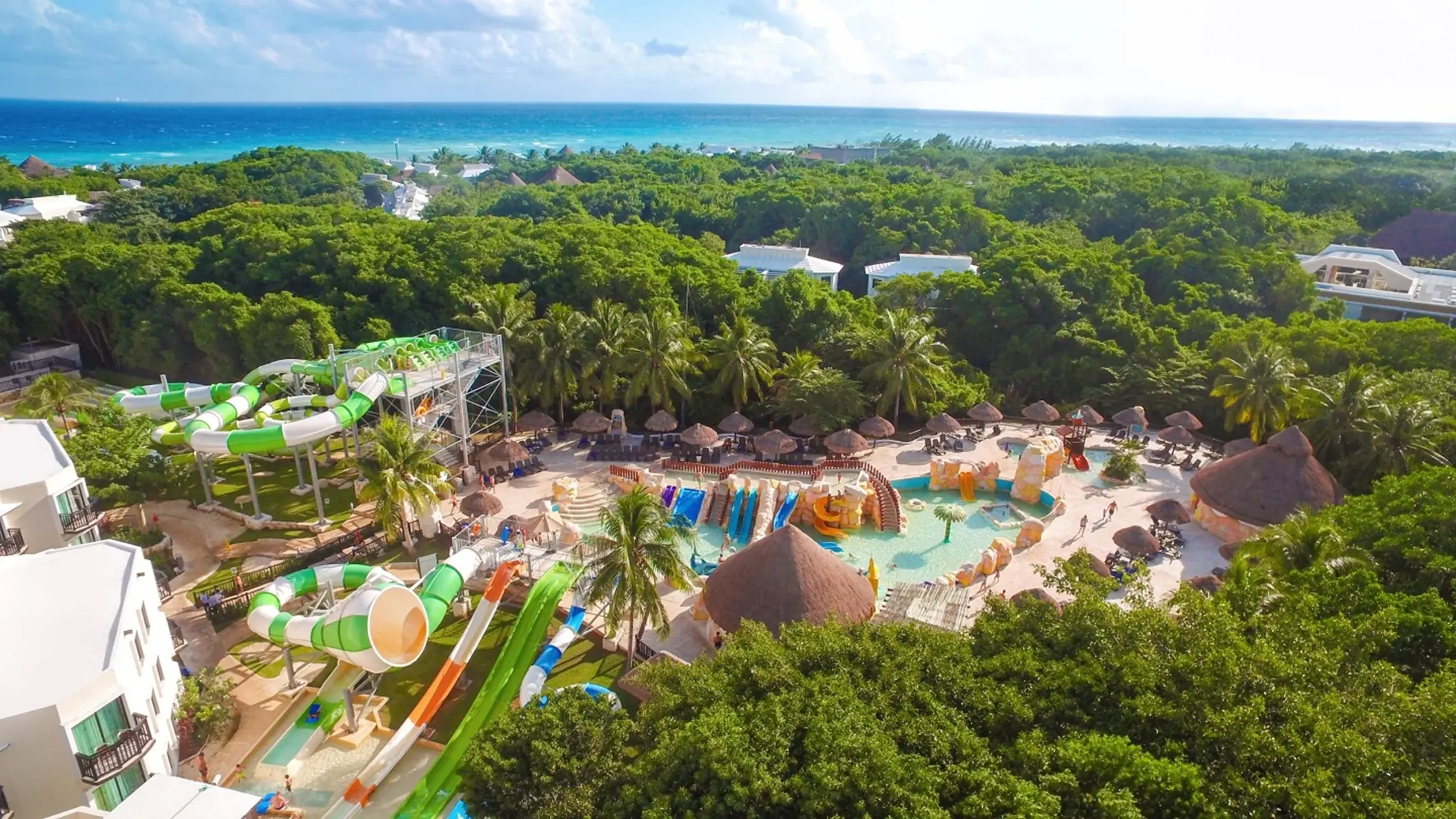 An aerial view of the vibrant water park at Sandos Caracol Eco Resort, surrounded by green nature and the ocean.