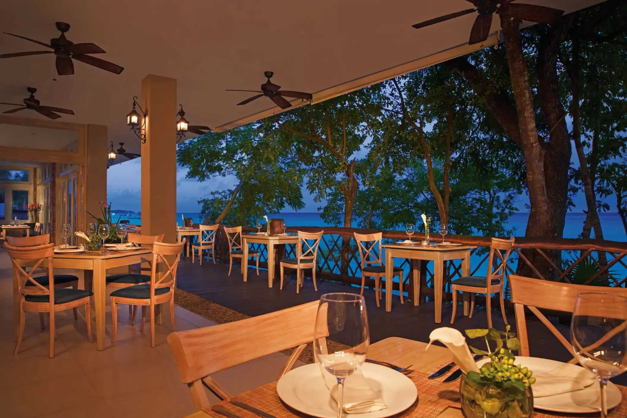 World Café terrace with open-air seating, tropical landscaping, and wooden accents overlooking lush greenery.