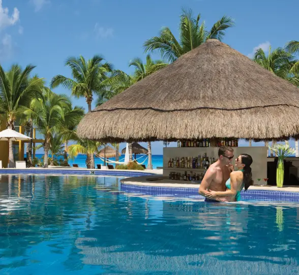 Thatched-roof pool bar with swim-up access and bar stools nestled within a tropical garden pool setting.