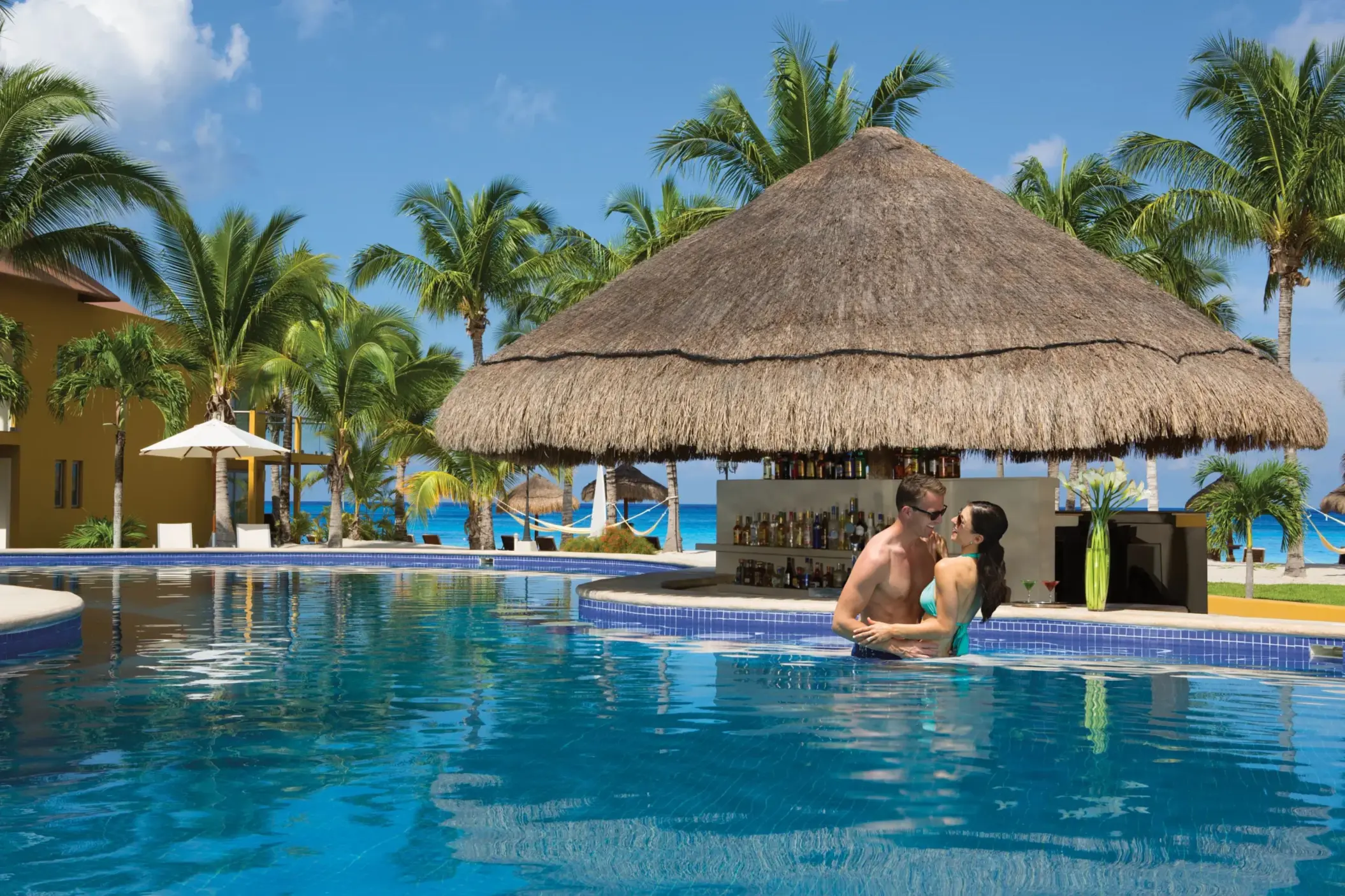 Thatched-roof pool bar with swim-up access and bar stools nestled within a tropical garden pool setting.