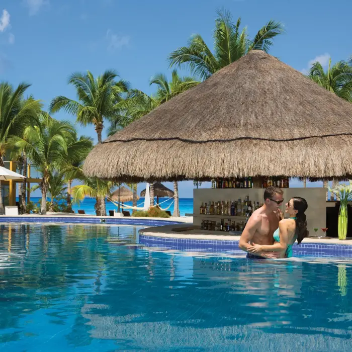 Thatched-roof pool bar with swim-up access and bar stools nestled within a tropical garden pool setting.