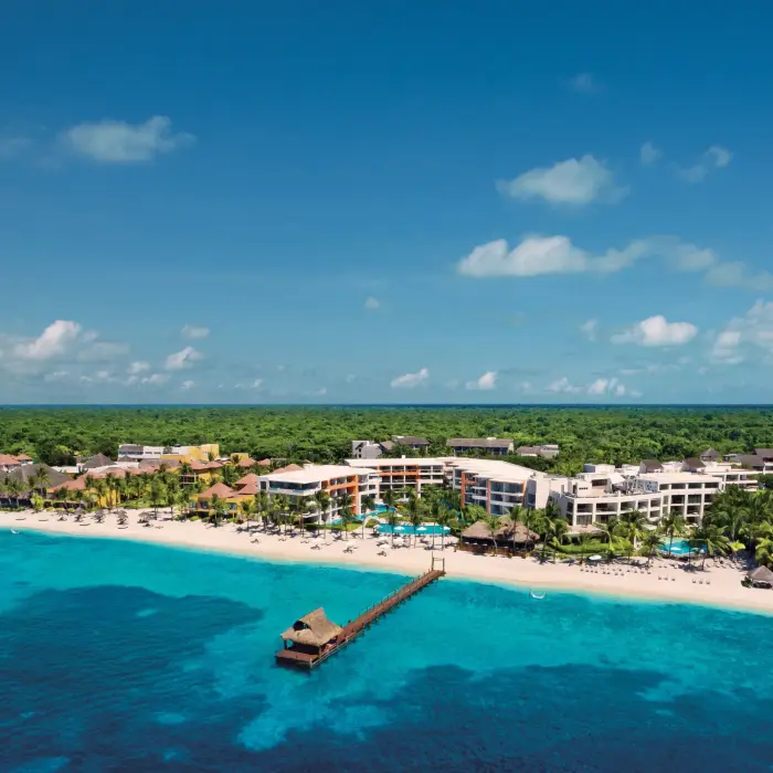 Stunning aerial view of the beachfront resort with pools, palm trees, and turquoise Caribbean shoreline.