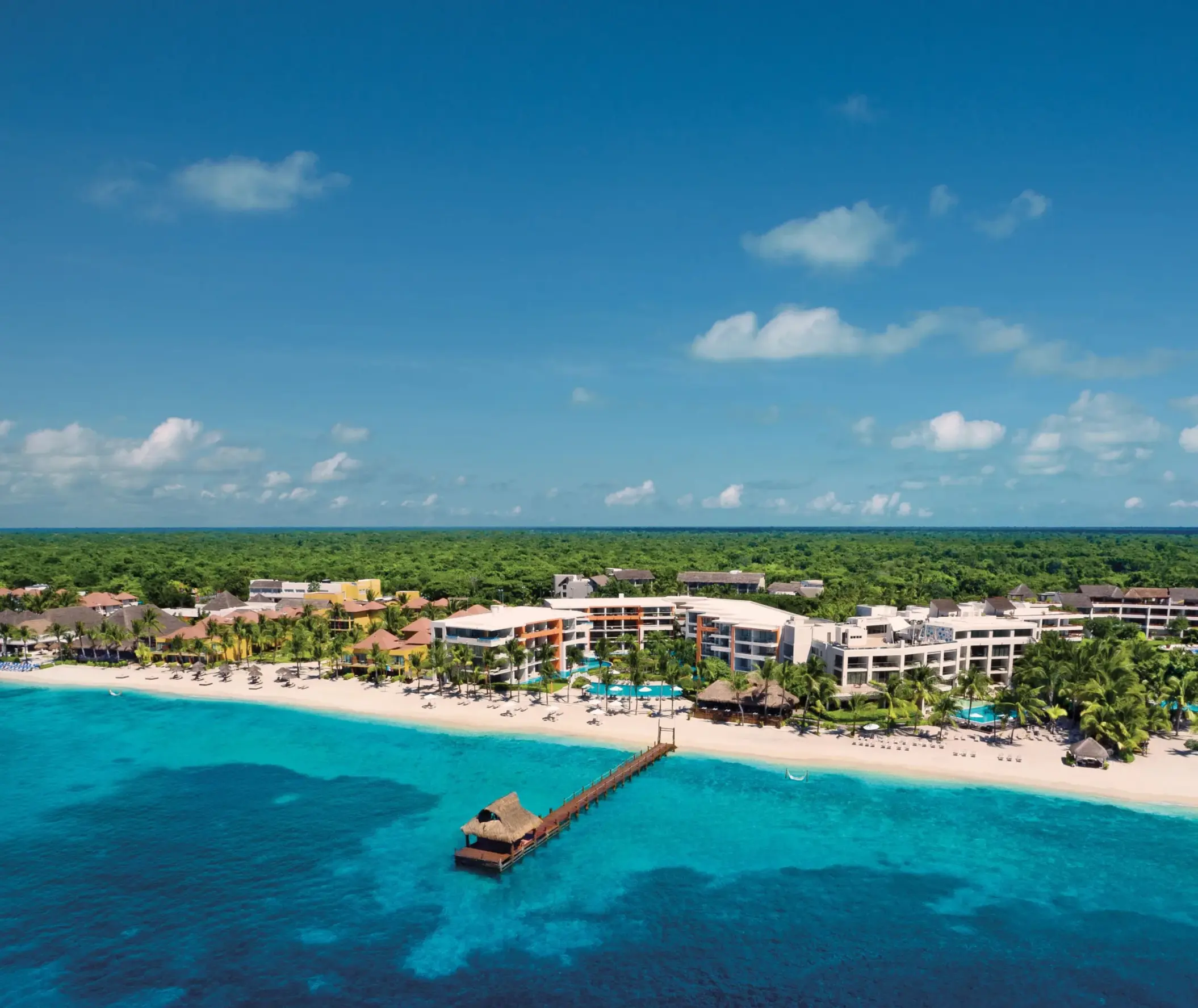 Stunning aerial view of the beachfront resort with pools, palm trees, and turquoise Caribbean shoreline.