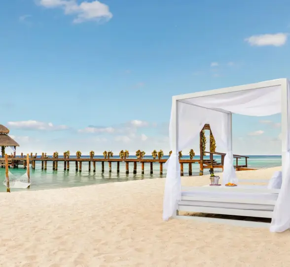 Luxurious beachside Bali bed with ocean views and a romantic pier stretching over calm blue water.