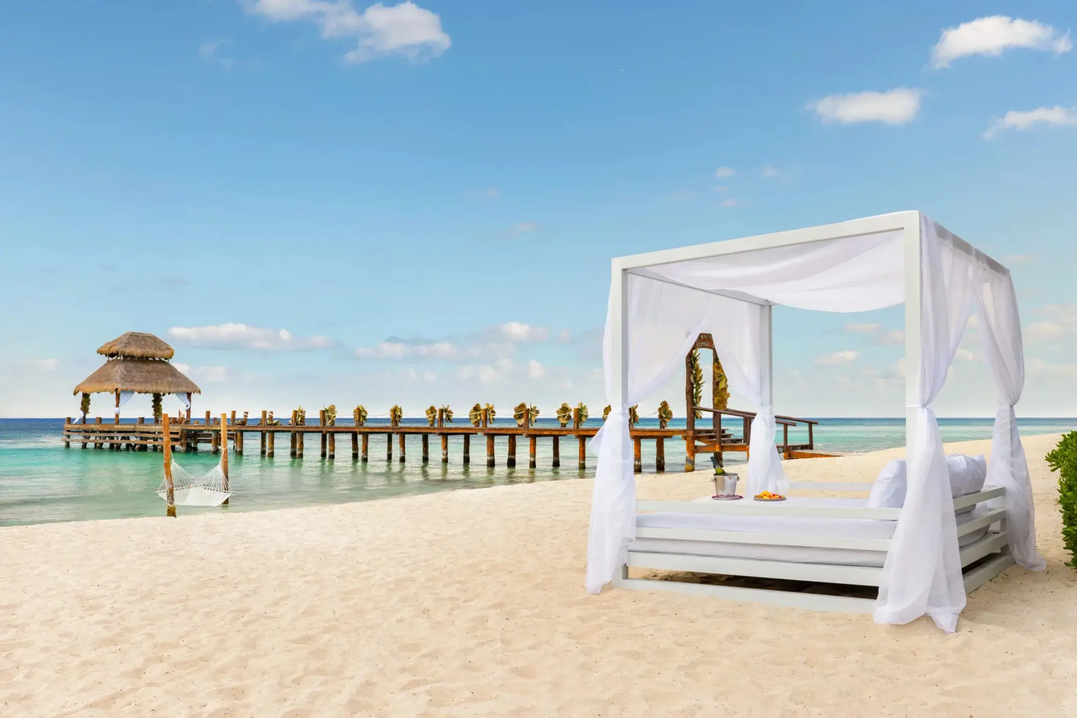 Luxurious beachside Bali bed with ocean views and a romantic pier stretching over calm blue water.