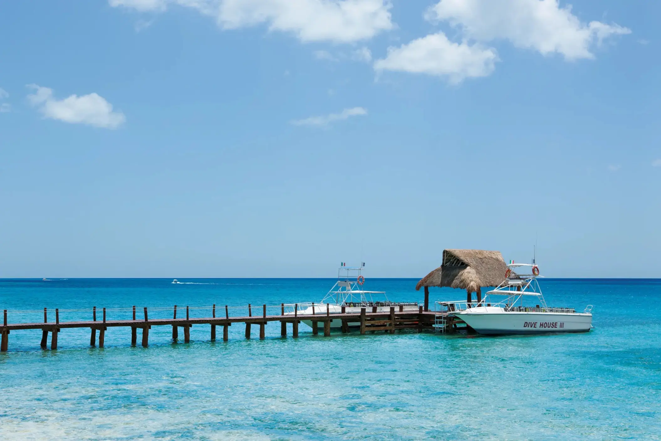 Dive boats docked at a thatched-roof pier on clear blue sea, ideal for scuba excursions.